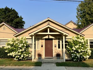 A two-story house with a brown front door, beige siding, and a gabled roof. There are two potted plants on the front porch. - Great downtown Sandpoint location! (Sandpoint)