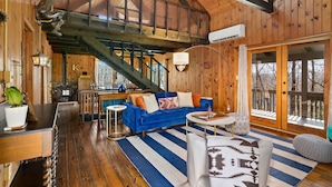 A spacious living area with a blue sofa, wooden flooring, and a staircase leading to an upper level. - Amazing Chalet Hot Tub Sauna Fire Pit Pet Friendly (Brevard)