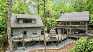 A two-story cabin with a deck and a stone fireplace, surrounded by dense forest. - Amazing Chalet Hot Tub Sauna Fire Pit Pet Friendly (Brevard)