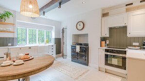A modern kitchen with a round wooden table, built-in appliances, and a large window. - Court Cottage - sleeps 8 guests  in 4 bedrooms (Painswick)