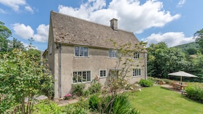 A two-story house with a tiled roof, surrounded by a well-maintained garden with various plants and flowers.