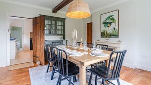 A dining room with a wooden table set for six, black chairs, a woven pendant light, and a green cabinet in the background. - Court Cottage - sleeps 8 guests  in 4 bedrooms (Painswick)