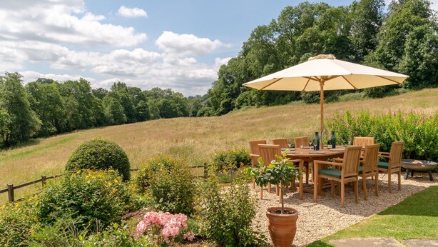 An outdoor dining area with a table and chairs, surrounded by a garden with various plants and flowers. - Court Cottage - sleeps 8 guests  in 4 bedrooms (Painswick)