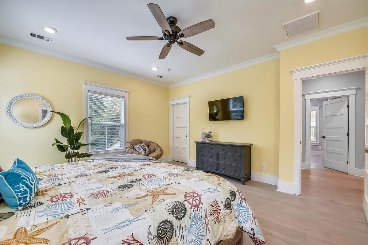 A bedroom with a bed, a ceiling fan, a dresser, a TV, and a window with blinds.