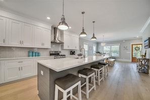 Une cuisine moderne avec des meubles blancs, un grand îlot central doté de tabourets, des appareils en acier inoxydable et un éclairage suspendu.