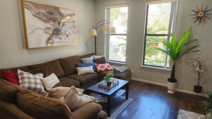 Ein Wohnzimmer mit braunem Sofa, einem Couchtisch und zwei Fenstern.