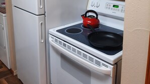 A kitchen with a white refrigerator, a stove with a red kettle, and wooden cabinets.
