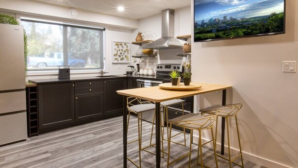 A modern kitchen with dark cabinets, a wooden table, and two gold chairs. - Contemporary Oasis in the Heart of Old Strathcona (Edmonton)
