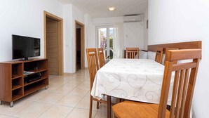 A dining area with a table set for four, wooden chairs, a TV on a stand, and a door leading outside. - Holiday apartment 100 m from the sea (Baška)
