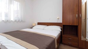 A bedroom with a bed, wooden wardrobe, and a nightstand with a lamp. - Holiday apartment 100 m from the sea (Baška)