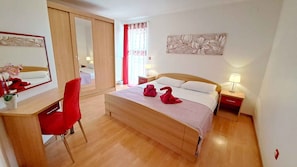 Ein Hotelzimmer mit einem hölzernen Bett, einem Schreibtisch mit Stuhl, einem Spiegel und einem roten Sessel.
