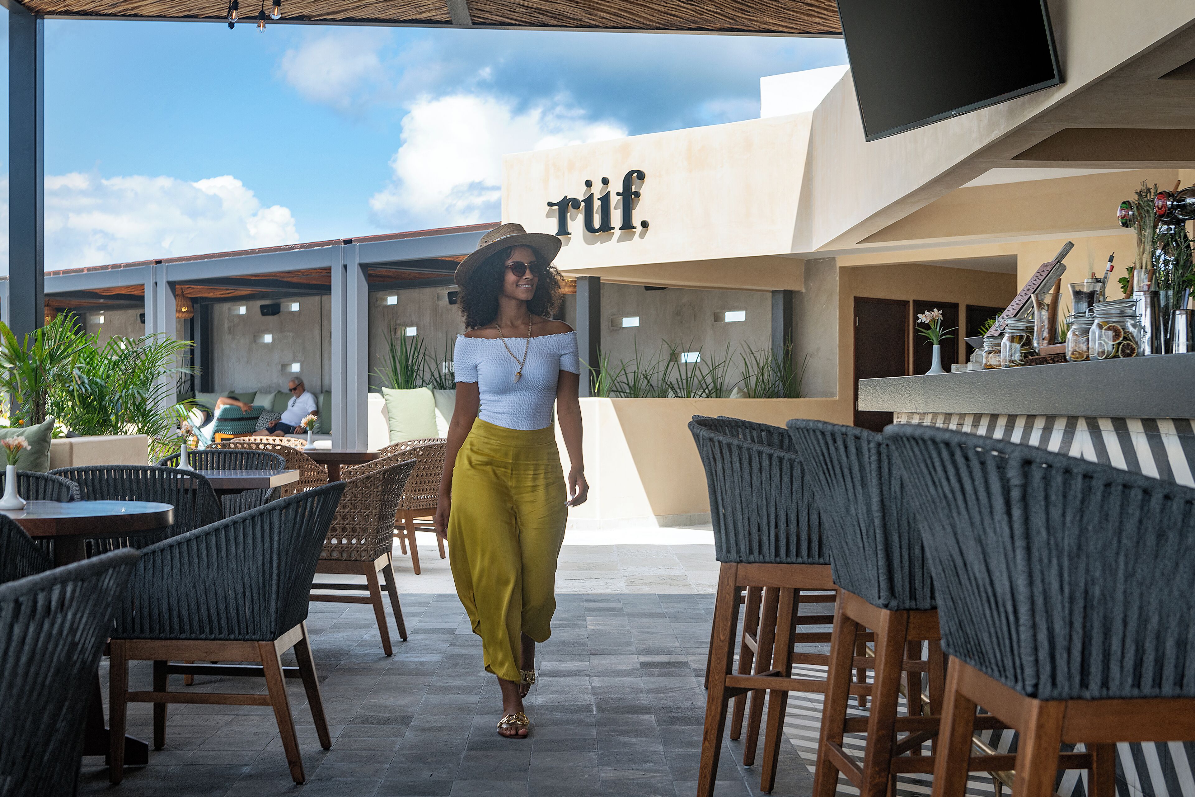 Un espace extérieur aménagé avec des chaises et des tables en osier, un téléviseur à écran plat fixé au mur et un panneau portant le mot « rif ».