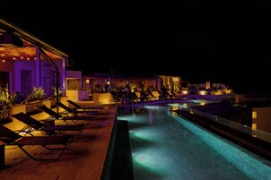 Un área de piscina nocturna con sillones de descanso y una piscina.
