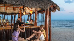 Eine Strandbar mit Holzmöbeln und einem Reetdach mit Blick auf das Meer.