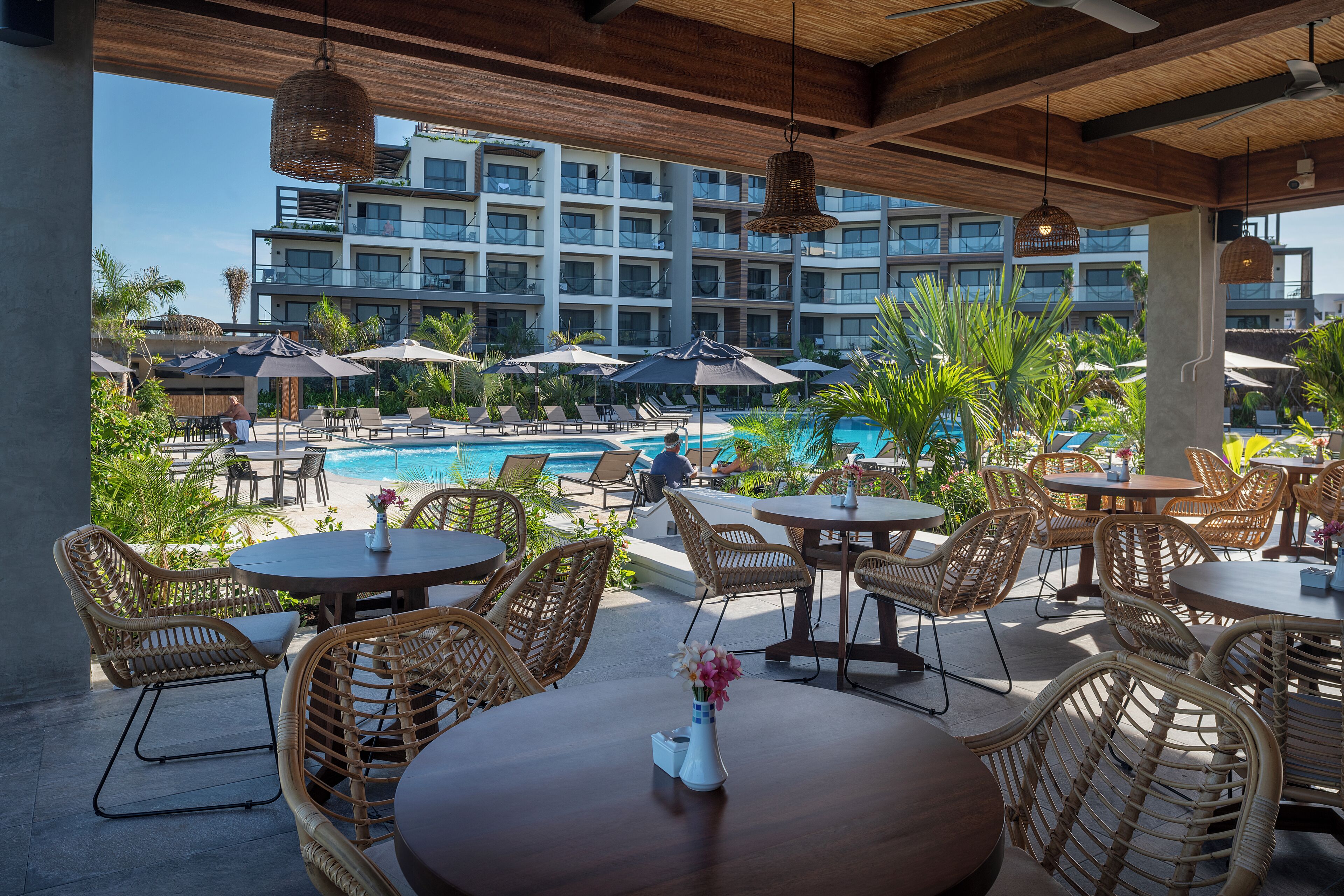 A poolside area with wicker furniture, umbrellas, and a view of a hotel building.