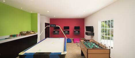 A room with a pool table, foosball table, and a TV mounted on the wall.