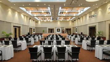 A large conference room with multiple tables and chairs, a stage, and a high ceiling with skylights.