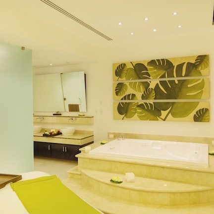 A modern bathroom with a large bathtub, a mirror, and a wall-mounted artwork of tropical leaves.