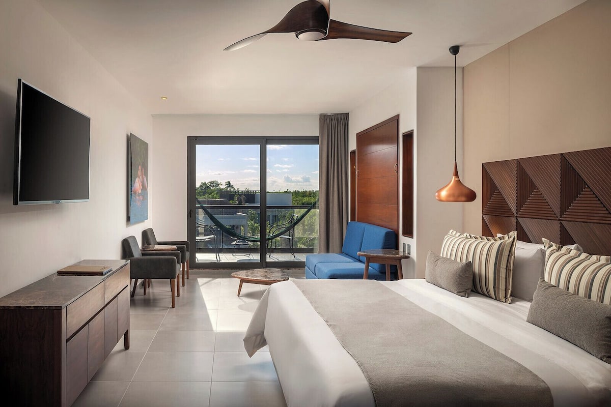 Une chambre d’hôtel moderne dotée d’un grand lit, d’un bureau, d’une chaise, d’un canapé et d’un balcon avec vue.
