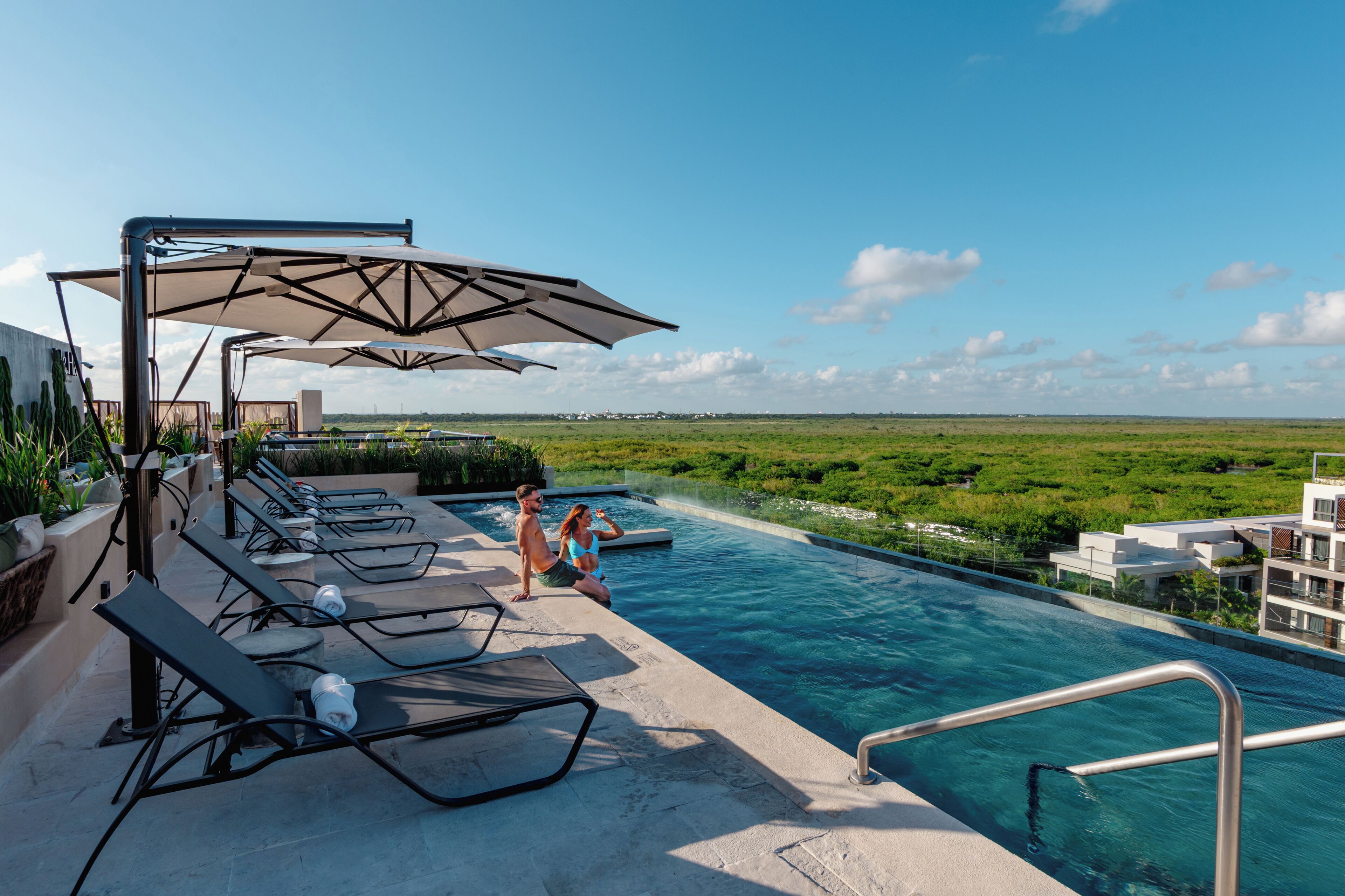 Un espace aménagé au bord de la piscine, avec des chaises longues et des parasols, un ciel dégagé et une vue sur la verdure.