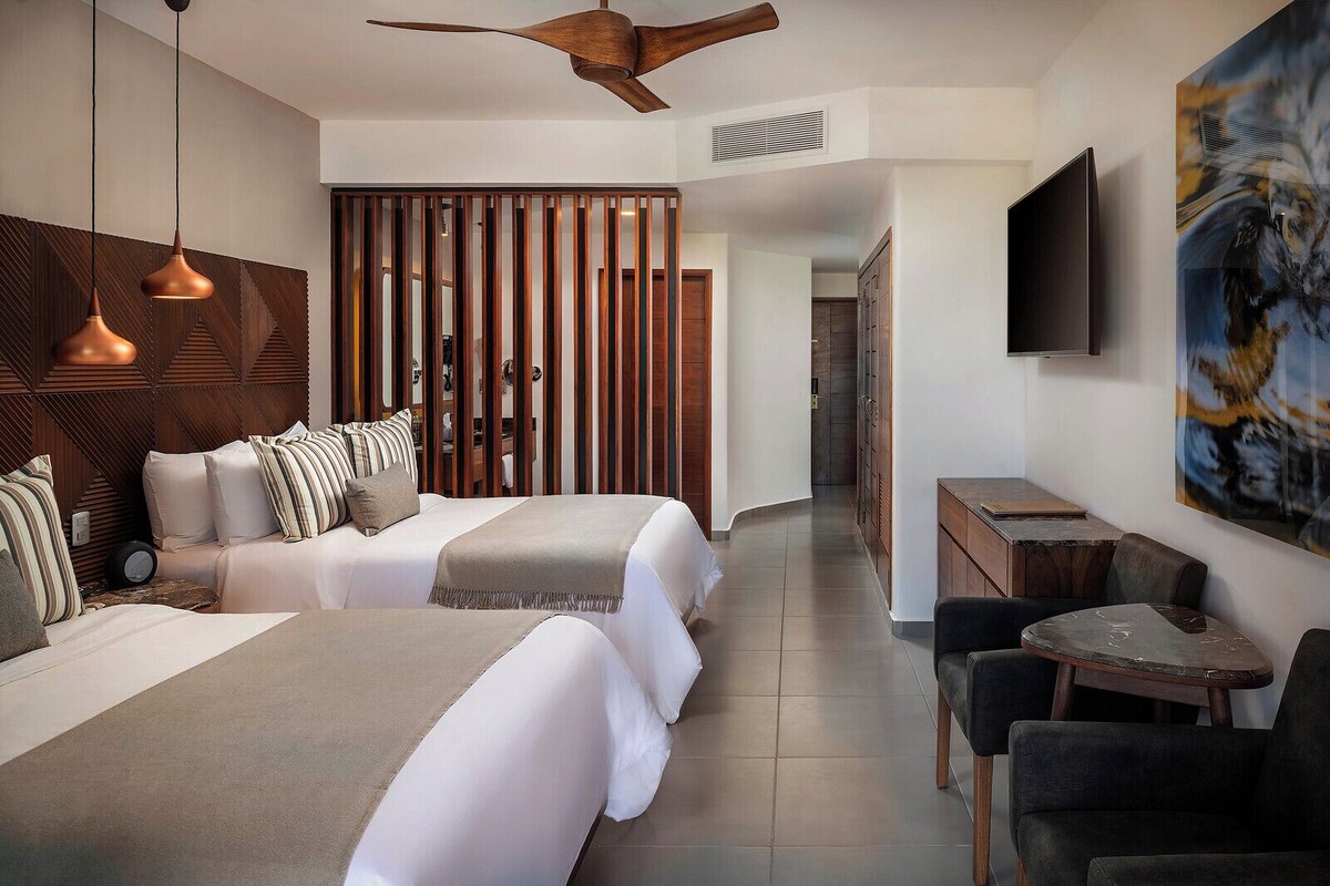 Une chambre d’hôtel moderne équipée d’un grand lit, d’un bureau, d’une chaise, d’une télévision et d’un ventilateur de plafond.