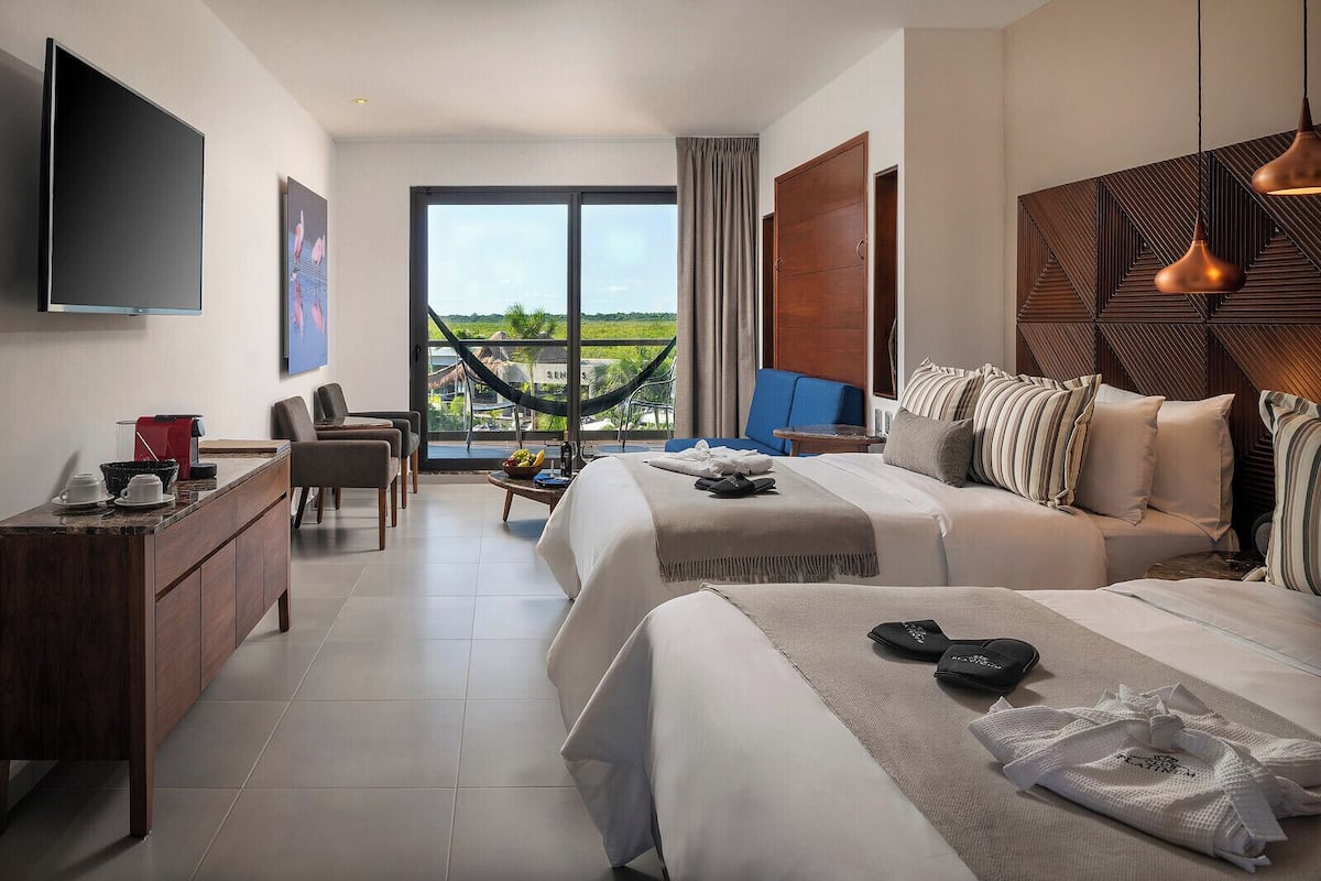 Une chambre d’hôtel comprenant un lit, un canapé, un bureau, une télévision et une vue sur un hamac et la verdure environnante.