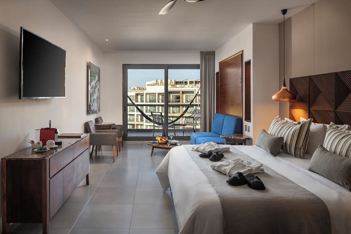 Une chambre d’hôtel moderne dotée d’un grand lit, d’un bureau, d’une télévision à écran plat, d’un balcon offrant une vue sur les bâtiments et d’un luminaire suspendu.