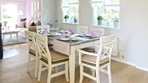 A dining area with a white table and chairs, a pink tablecloth, and potted plants by the windows.