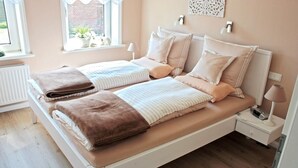 A double bed with a white frame, two pillows, and a brown blanket. There is a bedside table with a lamp and a phone.