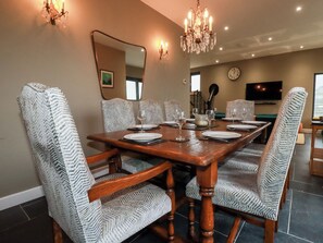 A dining area with a wooden table set for six, surrounded by patterned chairs, a chandelier, and a large mirror on the wall. - Postcard Lodge (Fowey)