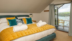 Une chambre à coucher avec un lit, des oreillers, une table de chevet, une lampe et une vue sur les bateaux, visible à travers une grande fenêtre.