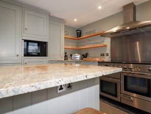 A modern kitchen with granite countertops, stainless steel appliances, and wooden shelves. - Postcard Lodge (Fowey)