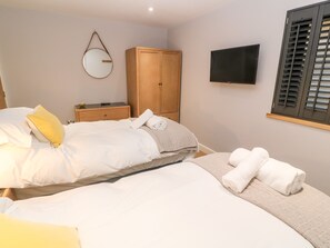 A bedroom with two beds, a wardrobe, a mirror, a television, and a window with blinds. - Postcard Lodge (Fowey)