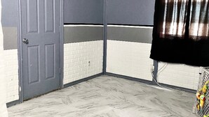 Een kamer met een grijze deur, witte bakstenen muren, een witte betegelde vloer en een zwart gordijn aan de rechterkant.