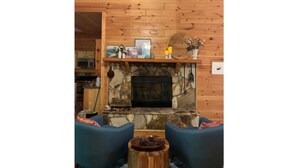 Ein gemütliches Wohnzimmer mit Kamin aus Stein, Holzwänden und blauen Sesseln.