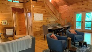 Ein gemütliches Blockhaus-Interieur mit einer Holztreppe, einer Essecke und einem Wohnzimmer mit Sofa und Sesseln.
