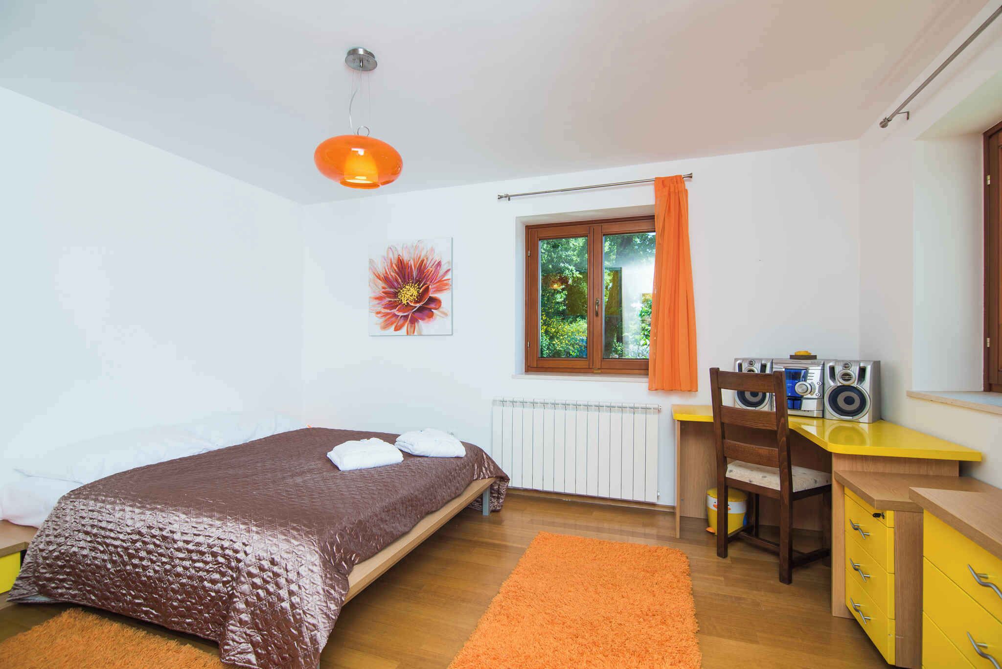 A bedroom with a bed, a desk with a chair, a radiator, and a window with curtains.