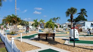 Ein Golfplatz mit weißem Zaun, Palmen und einer Bank.