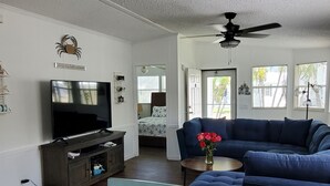 Ein Wohnzimmer mit Fernseher, einem blauen Sofa und einem Essbereich mit einem Holztisch.