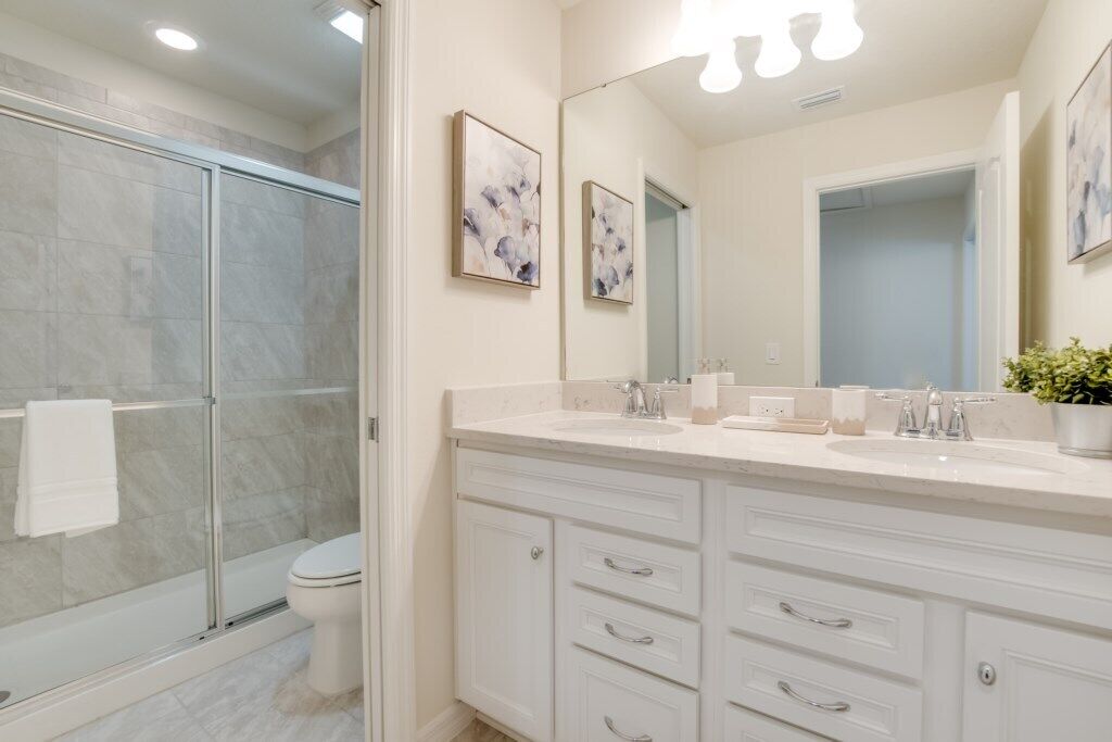 A modern bathroom with a glass shower enclosure, a white sink vanity with two basins, and a large mirror above the vanity.