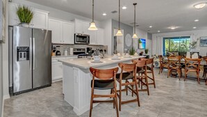 Una cocina moderna con armarios blancos, electrodomésticos de acero inoxidable y una isla central con taburetes de bar.