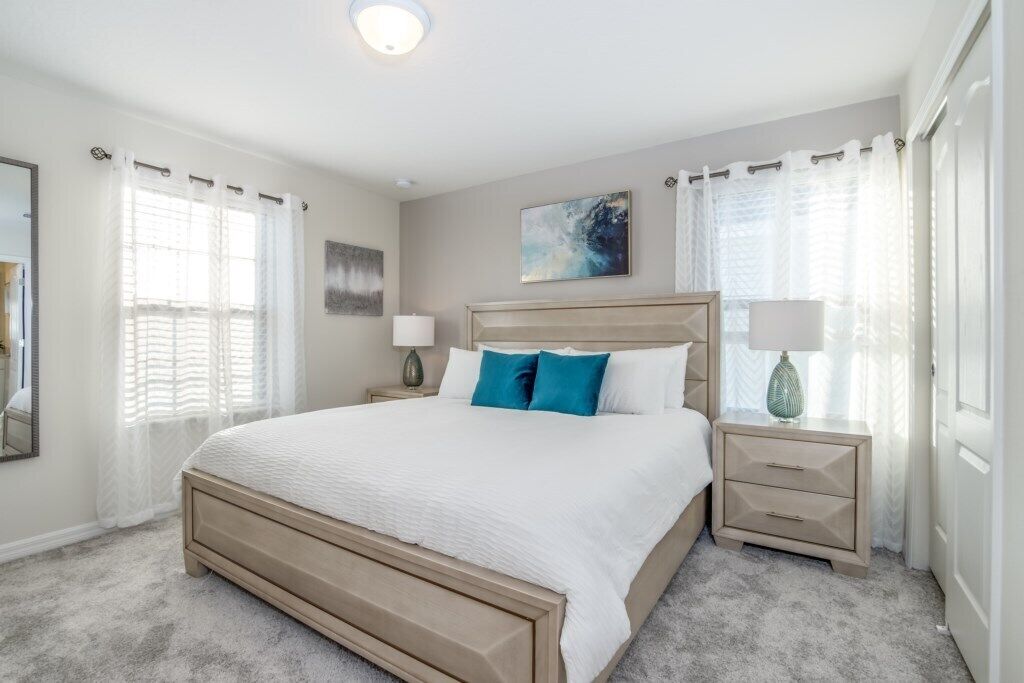 A bedroom with a large bed, two bedside tables, a nightstand, and a window with curtains.