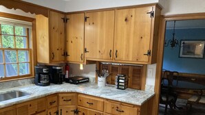 A kitchen with wooden cabinets, a coffee maker, a spice rack, and a window with blinds. -  Downtown Edgartown Historic District. Walk to town and harbor. (Edgartown)