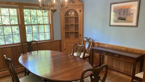 A dining room with a wooden table and chairs, a chandelier, and a cabinet with glass doors. -  Downtown Edgartown Historic District. Walk to town and harbor. (Edgartown)