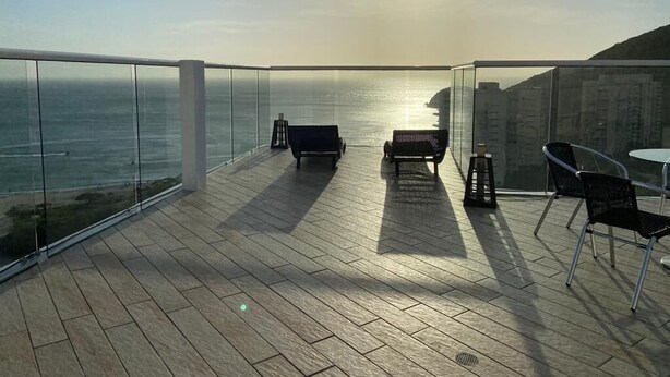 Un balcón con vista al océano, piso de madera y mobiliario exterior.