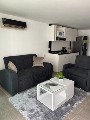 A modern living room with a black sofa, a glass coffee table, and a grey furry rug. - Apartamento (Santa Marta)