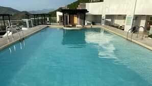 Una piscina con agua azul cristalina, un área de descanso techada y una vista de montañas al fondo.