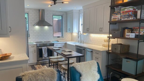 Une cuisine moderne avec des meubles blancs, un îlot central et un coin repas avec des chaises bleues.