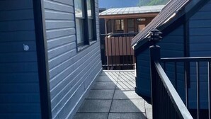 Un étroit couloir extérieur doté d’une rambarde en métal, qui mène à une terrasse en bois offrant une vue sur les montagnes.