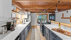 A modern kitchen with wooden beams, a large island, and a view to the outside. - Beautiful chalet on 5 acres - 2 min to Village!👌 Hot-Tub, Sauna, Fire Pit🔥 (Ellicottville)